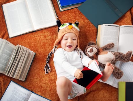 One year old baby in owl hat reading books with teddy bear