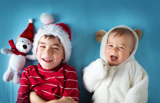 Two brothers, one and six years old in santa and bear costumes lying on blue blanket