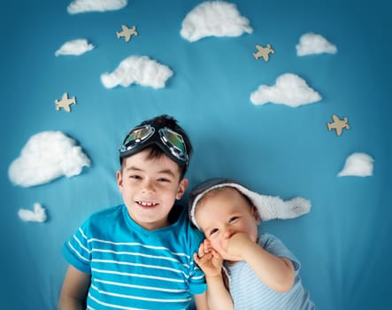 Two boys lying on blanket with white clouds in pilot hat and glasses
