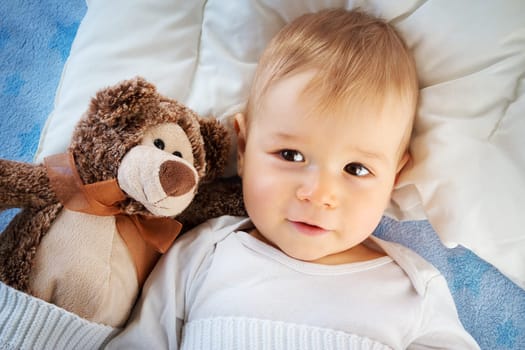 One year old baby lying in bed with a plush teddy bear