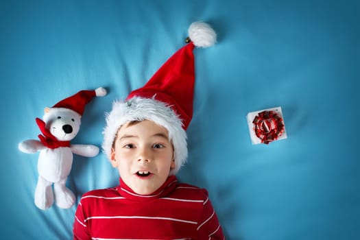 Happy boy in santa claus hat with a white bear on blue blanket