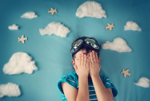 boy lying on blanket with white clouds in pilot glasses