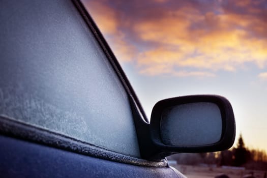 Car window and side mirror covered with ice in early morning