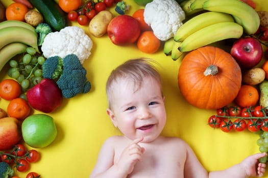 baby surrounded with fruits and vegetables on yellow blanket, healthy child nutrition
