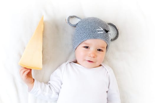 Baby boy in mouse hat lying on blanket with big piece of cheese