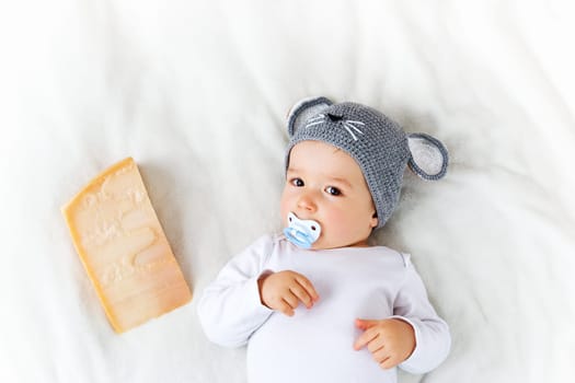 Baby boy in mouse hat lying on blanket with big piece of cheese