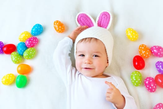 Baby boy in bunny hat lying on green blanket with multicolored easter eggs