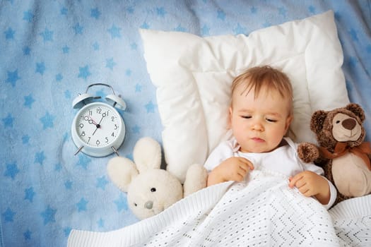 One year old baby lying in bed with alarm clock