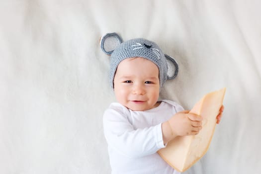 Baby boy in mouse hat lying on blanket with big piece of cheese