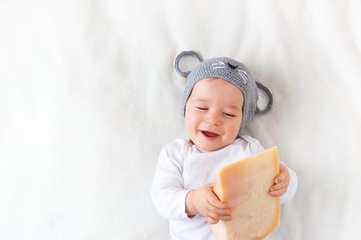 Baby boy in mouse hat lying on blanket with big piece of cheese