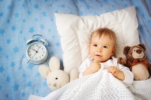 One year old baby lying in bed with alarm clock