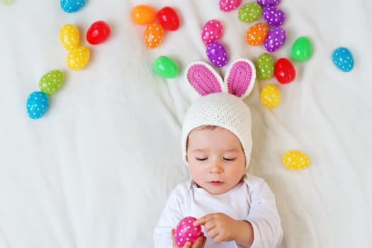 Baby boy in bunny hat lying on green blanket with multicolored easter eggs