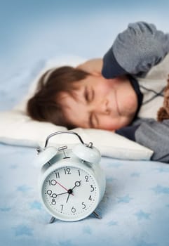 six years old child sleeping in bed on pillow with alarm clock and a teddy bear