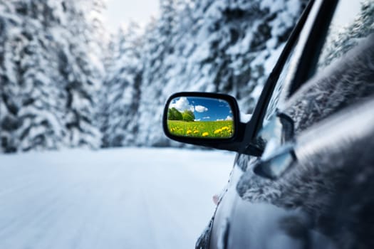 car on winter road with summer field reflection in mirror