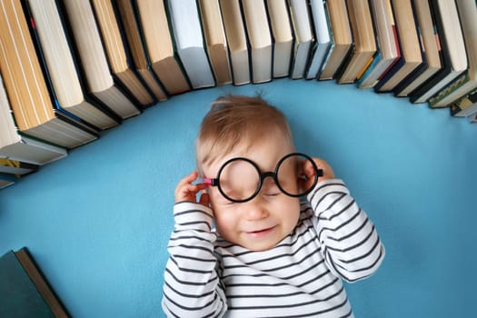 One year old baby among books with spectackle