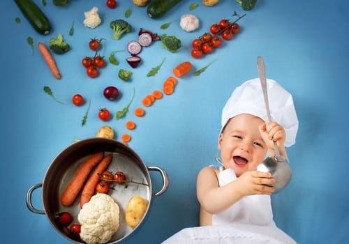 Baby boy in chef hat with cooking pan and raw vegetables