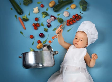 Baby boy in chef hat with cooking pan and raw vegetables