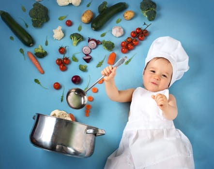 Baby boy in chef hat with cooking pan and raw vegetables
