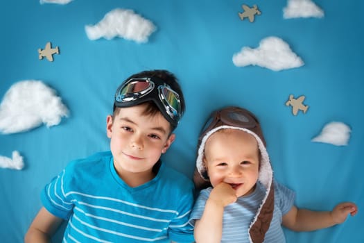 Two boys lying on blanket with white clouds in pilot hat and glasses