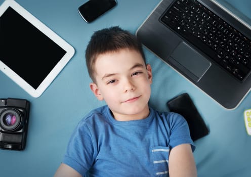 seven years old boy on blue blanket background with laptop, tablet, camera and phones