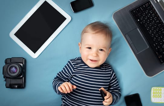 little boy on blue blanket background with laptop, tablet, camera and phones