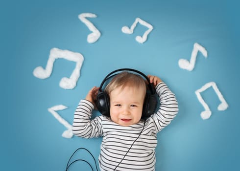 happy little boy on blue blanket background with headphones and musical notes on blue background
