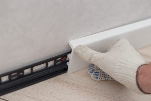 Man putting new skirting board or floor baseboard on wall in house.