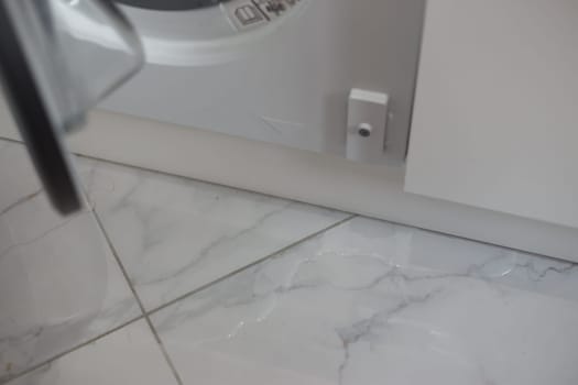 Spilled water leaked from washing machine built into the kitchen furniture. Spilled water on the tiled floor, flooding