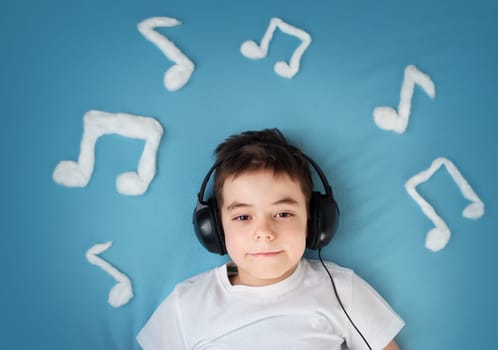 happy little boy on blue blanket background with headphones and musical notes on blue background