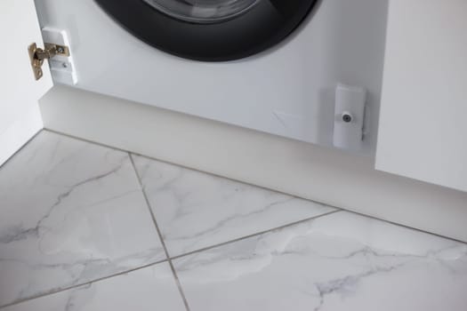 Spilled water leaked from washing machine built into the kitchen furniture. Spilled water on the tiled floor, flooding