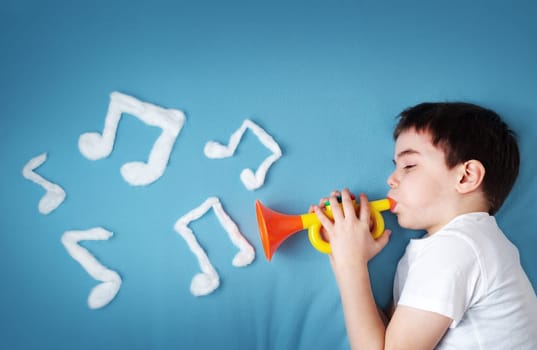 happy seven years old boy on blue blanket background with pipe and musical notes on blue background