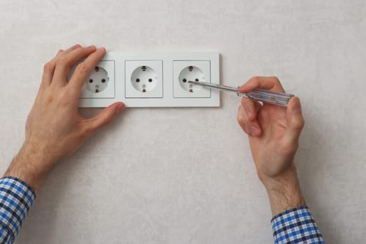 Hand of electrician using phase tester screwdriver to repair wall socket.