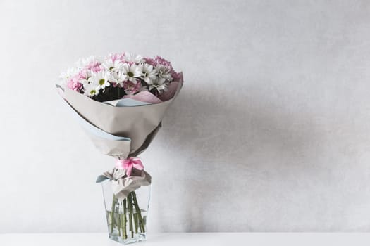 Bouquet of white and pink chrysanthemums in glass vase on table.