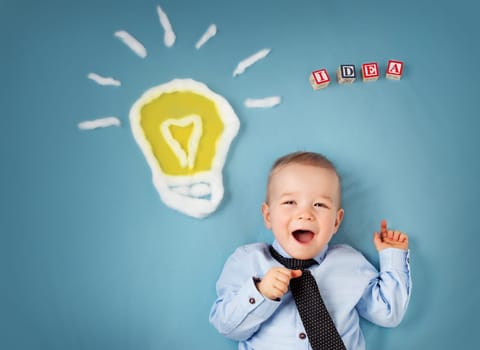 One year old boy with a bulb on blue background. Child with an idea
