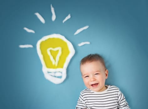 One year old boy with a bulb on blue background. Child with an idea
