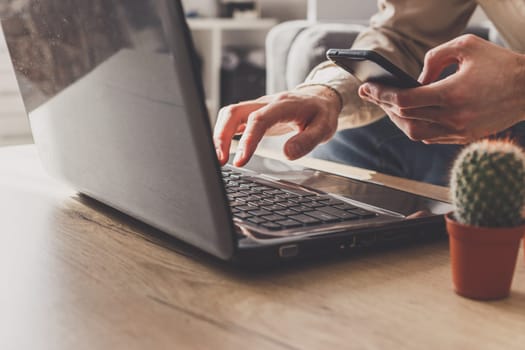 Close up of business man working on laptop computer and smartphone, sending email working from home.