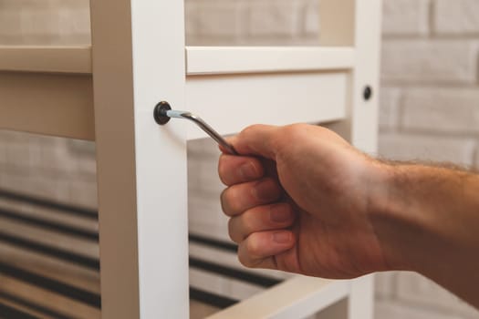 Assembling of furniture, closeup hex wrench in hand, furniture screw screwed into board of bench.