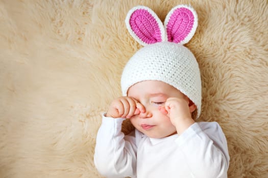 sleepy one year old baby lying in bunny hat on lamb wool background