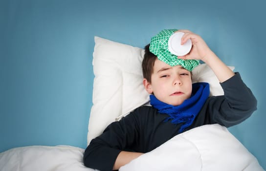 Ill boy lying in bed. sad child with fever and ice bag on head