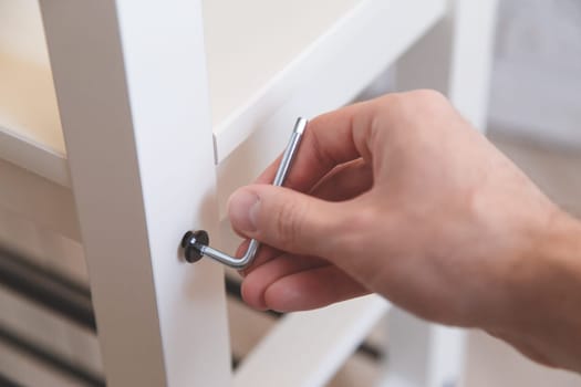 Assembling of furniture, closeup hex wrench in hand, furniture screw screwed into board of bench.