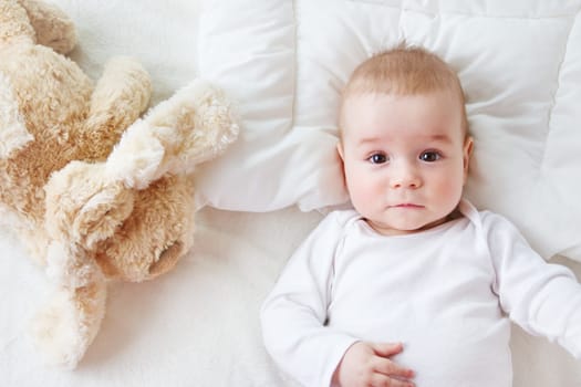 seven month old boy lying in the bed with a plush dog toy