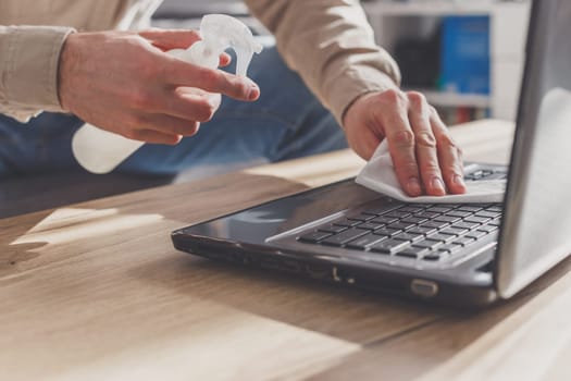 Man disinfects his laptop, cleaning keyboard. Wiping by rubbing alcohol spray and disinfectant.