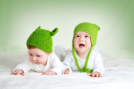 two cute six month old babies lying in frog hats on soft blanket