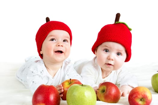 two cute six month old babies lying in hats on soft blanket with apples