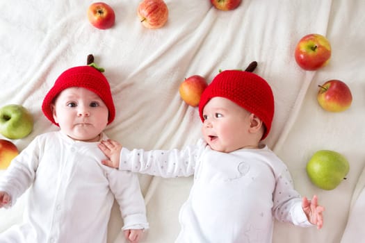 two cute six month old babies lying in hats on soft blanket with apples