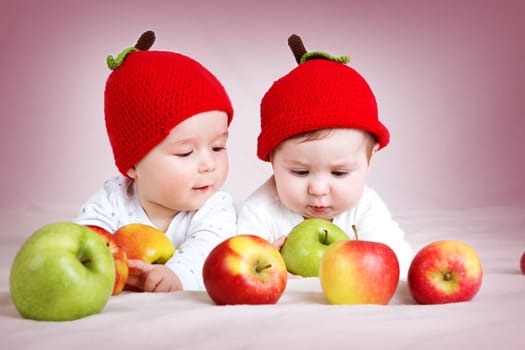two cute six month old babies lying in hats on soft blanket with apples