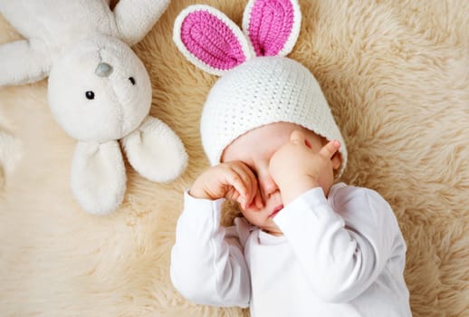 sleepy one year old baby lying in bunny hat on lamb wool background