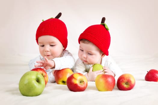 two cute six month old babies lying in hats on soft blanket with apples