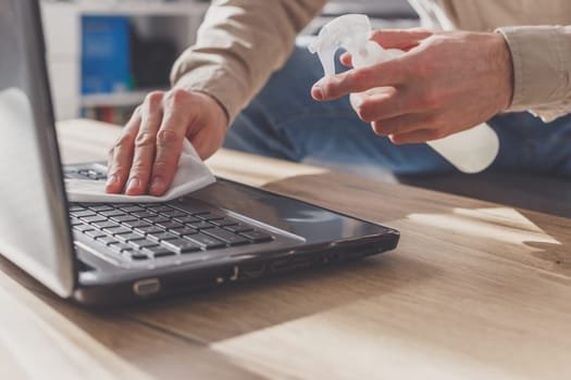 Man disinfects his laptop, cleaning keyboard . Wipe with rubbing alcohol spray and disinfectant.
