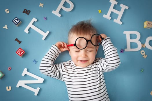 One year old child lying with spectacles and letters on blue background